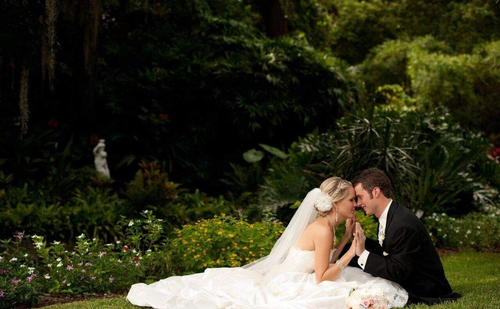 Bride and groom kissing on a white blanket in a lush garden setting