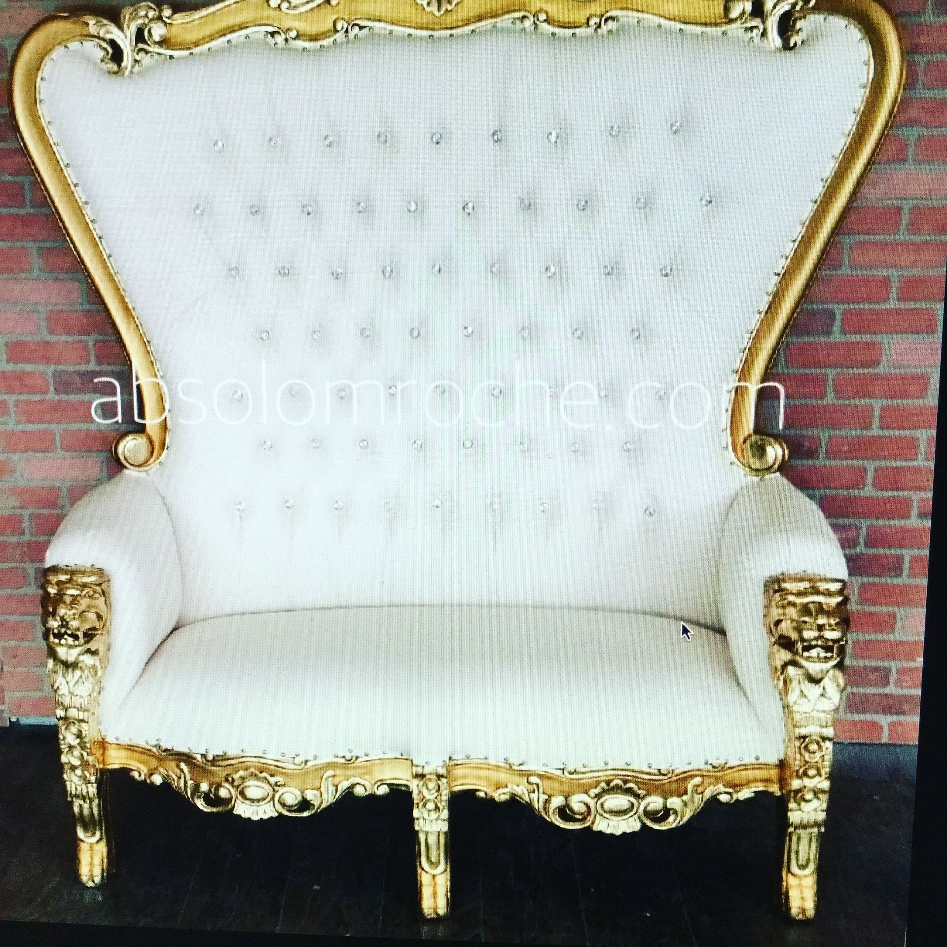 White tufted Victorian-style armchair with ornate gold trim, shown against a red brick wall