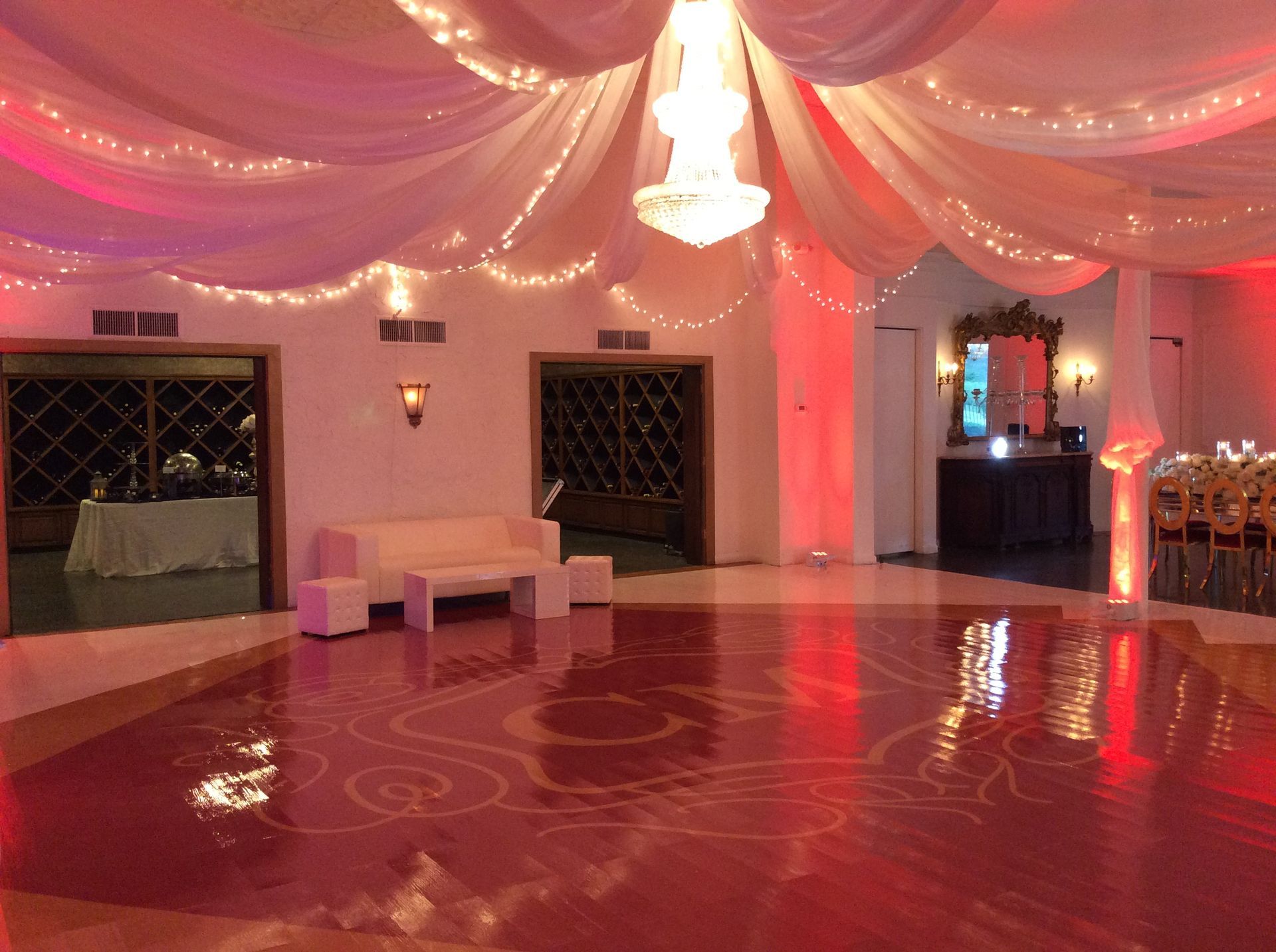 Elegant event hall with white draped ceiling, pink lighting, red glossy dance floor, and white seating area