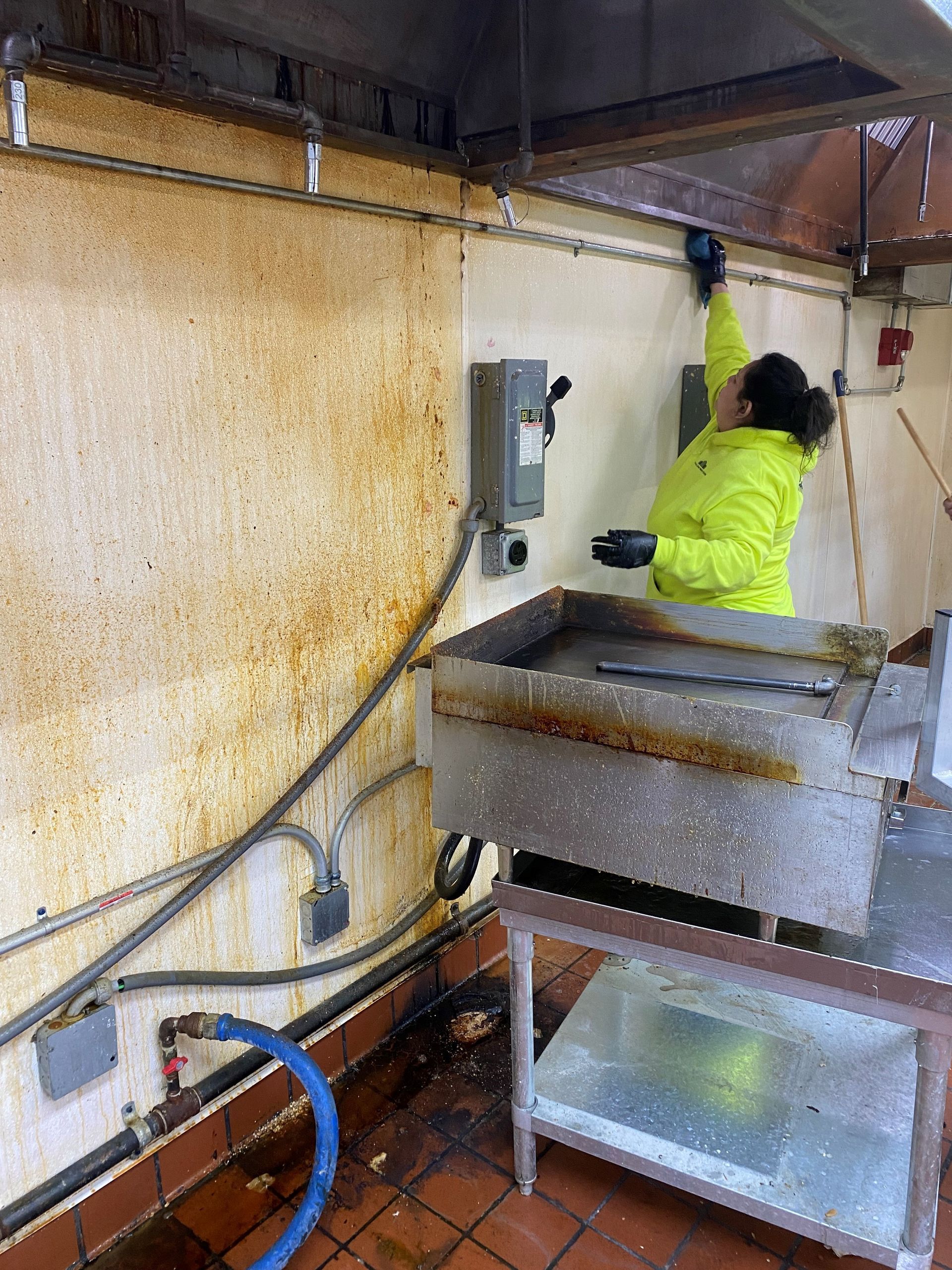A woman is cleaning a dirty kitchen with a hose.
