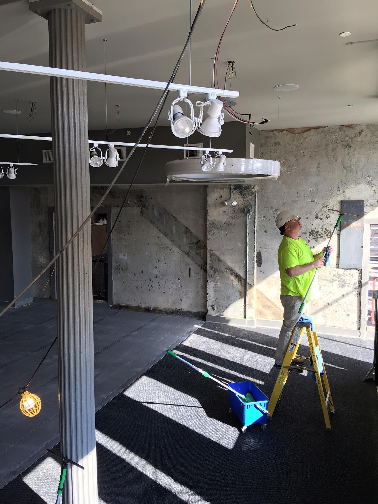 A man is standing on a ladder cleaning a window in an empty room.