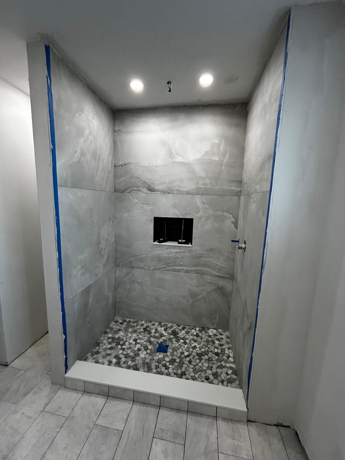 a newly tiled shower stall with gray stone pebble flooring and large gray tiles on the walls