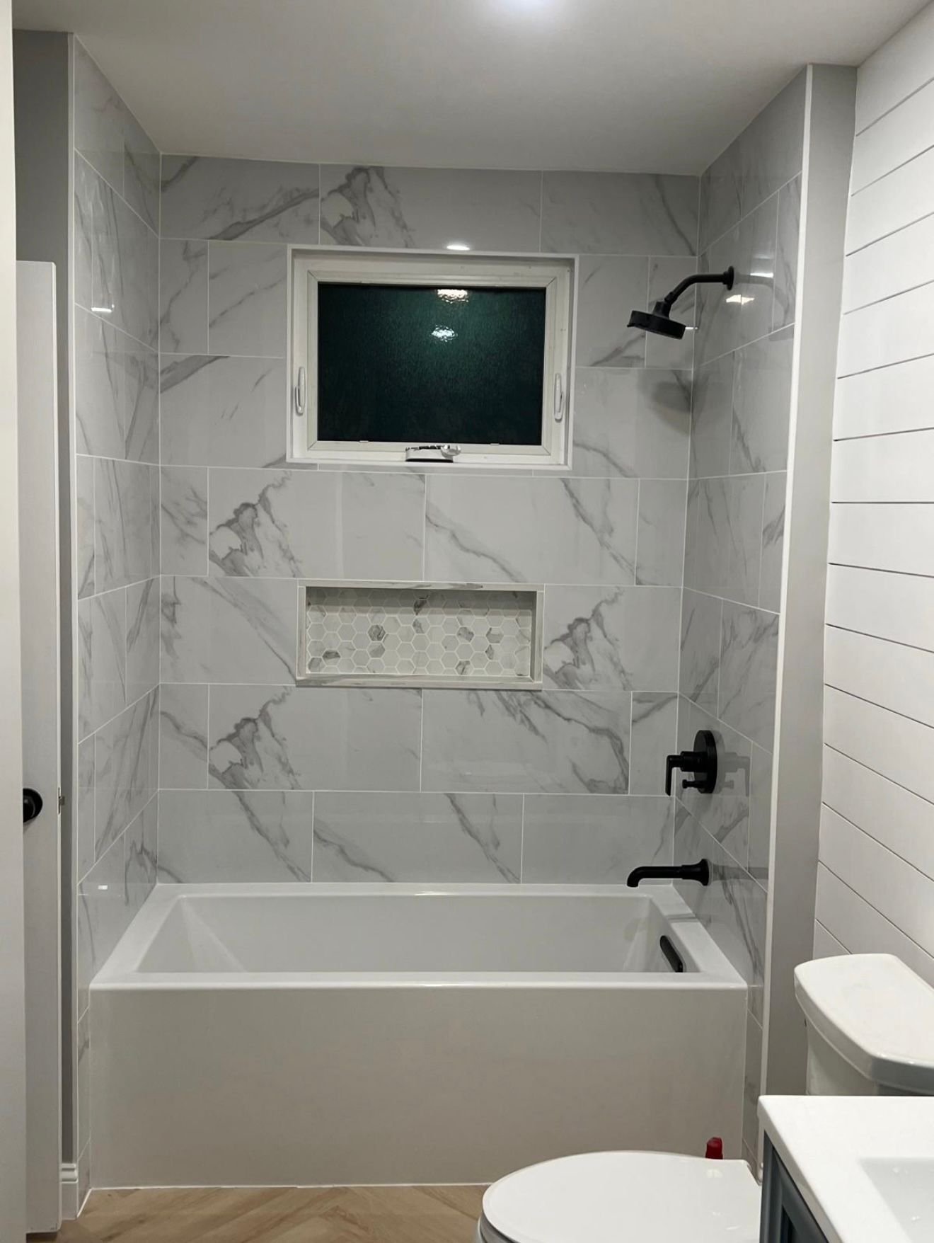 a bathroom with white tub, marble tile shower, black fixtures, and a window
