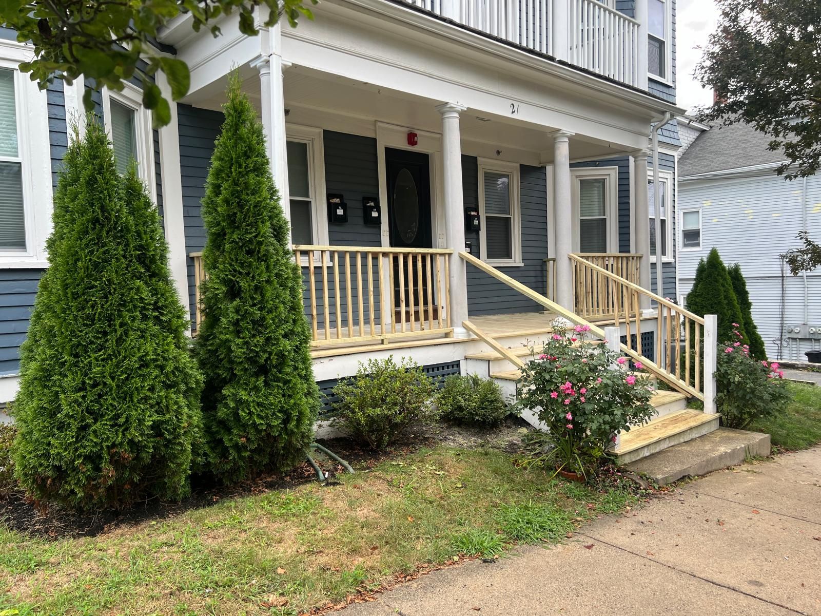 A house with a porch and stairs is surrounded by trees and bushes.