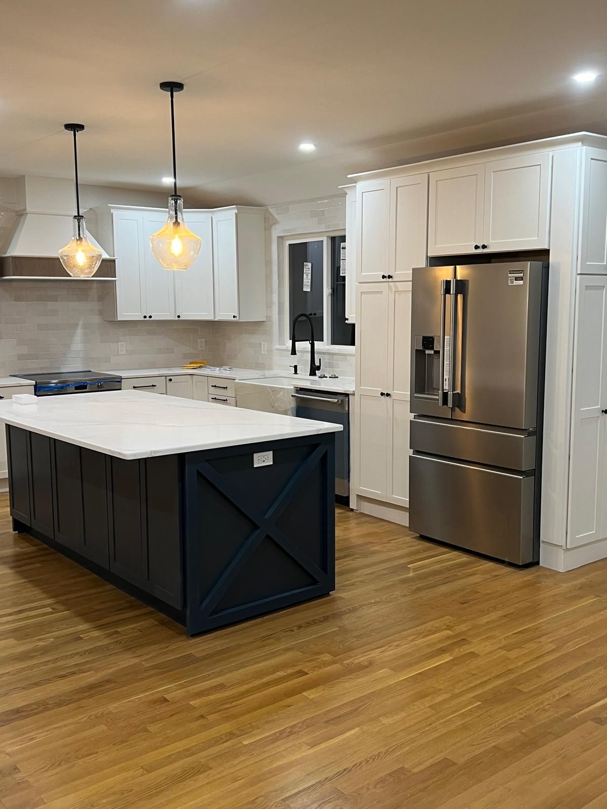 A kitchen with a large island, stainless steel refrigerator, and white cabinets.