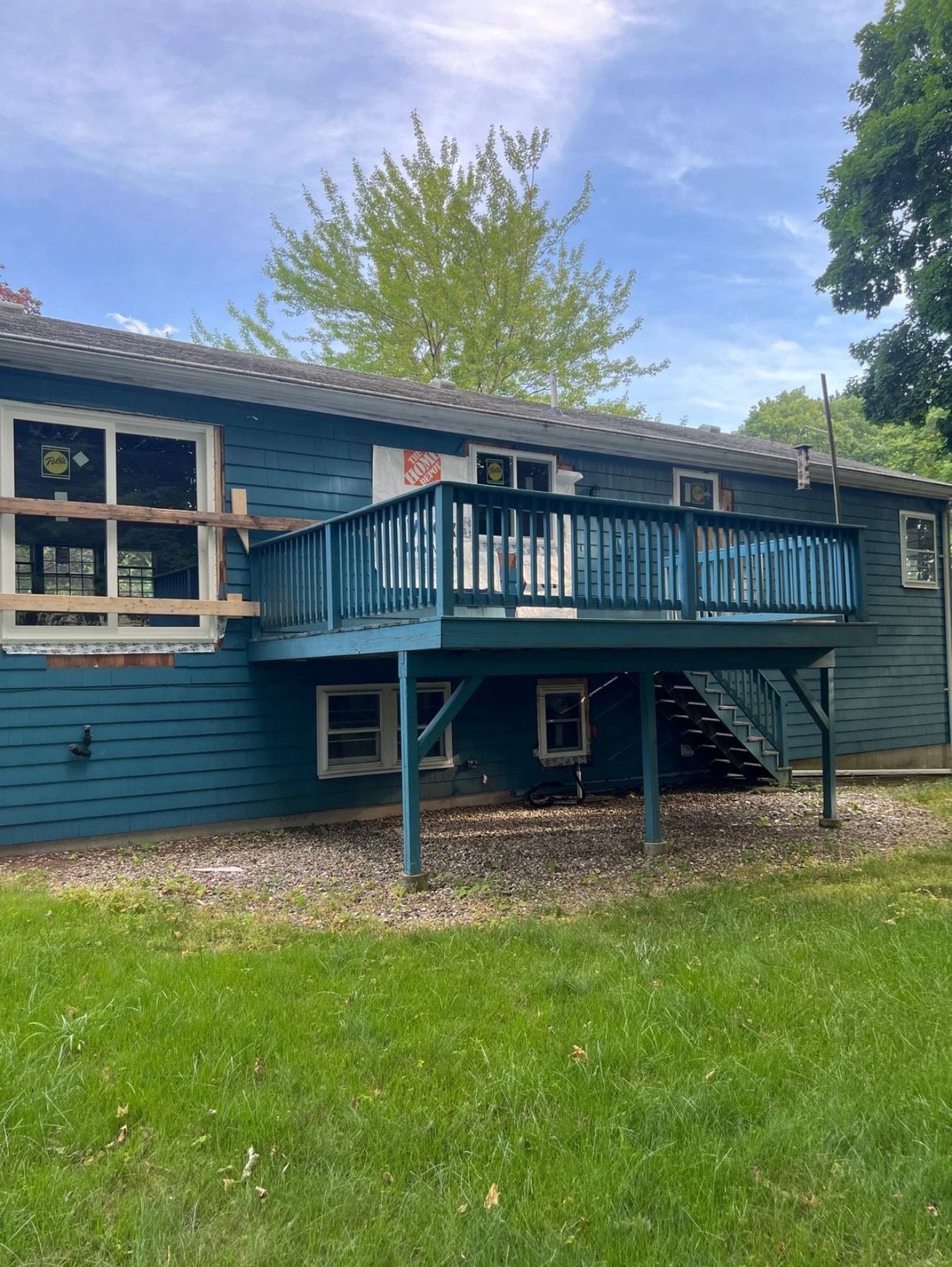 A blue house with a wooden deck and stairs leading down to a grassy yard on a sunny day.