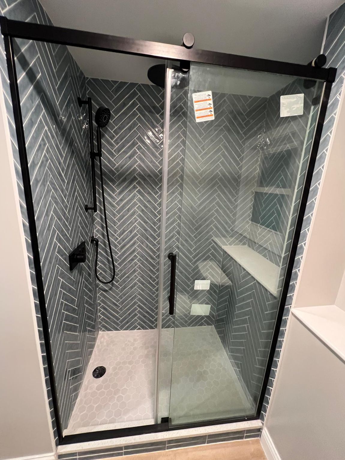 A bathroom with a sliding glass shower door and a herringbone tile wall.