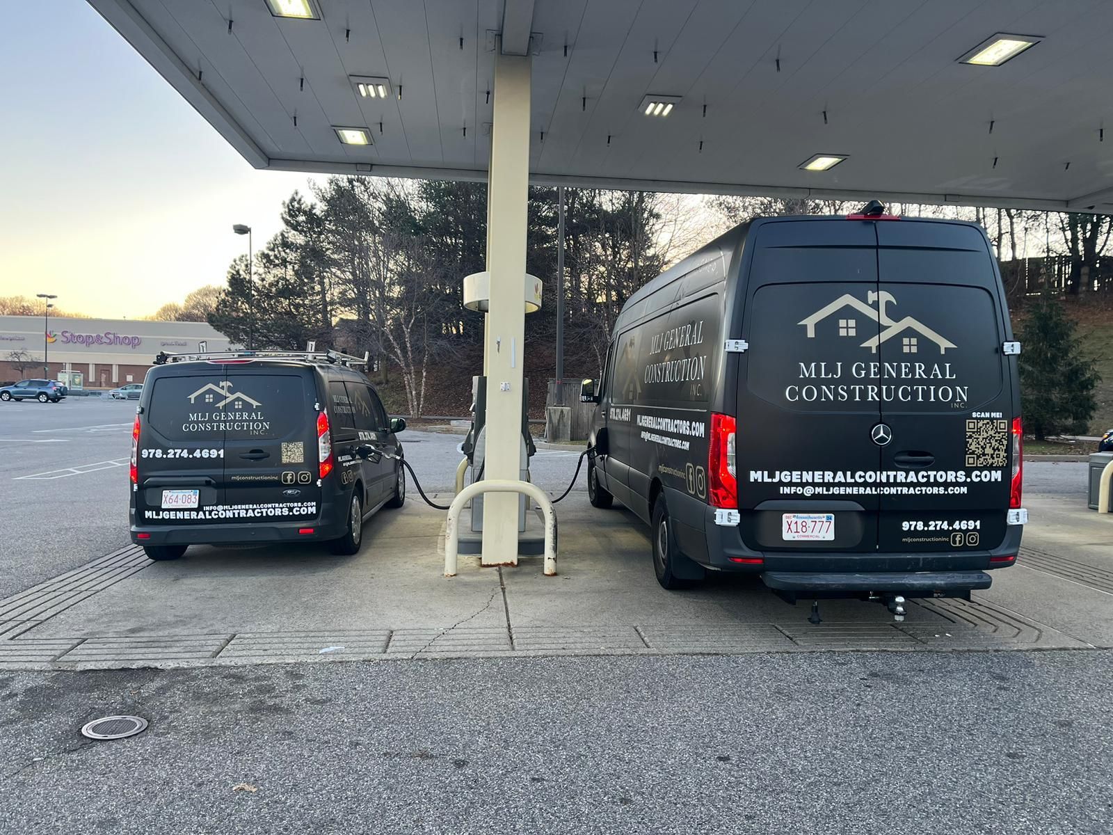 Two vans are parked under a canopy at a gas station