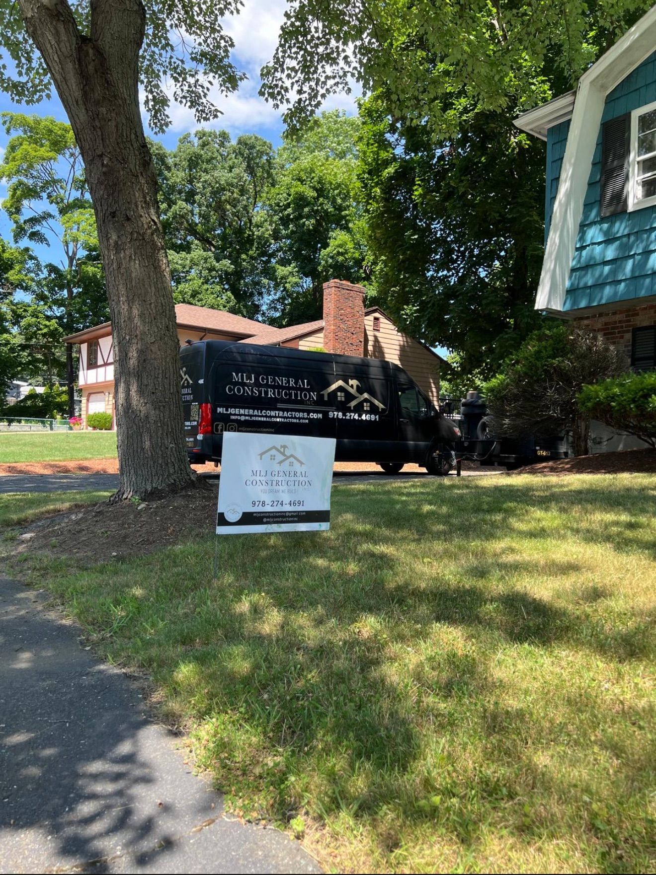A black van is parked in front of a house with a sign in the grass.
