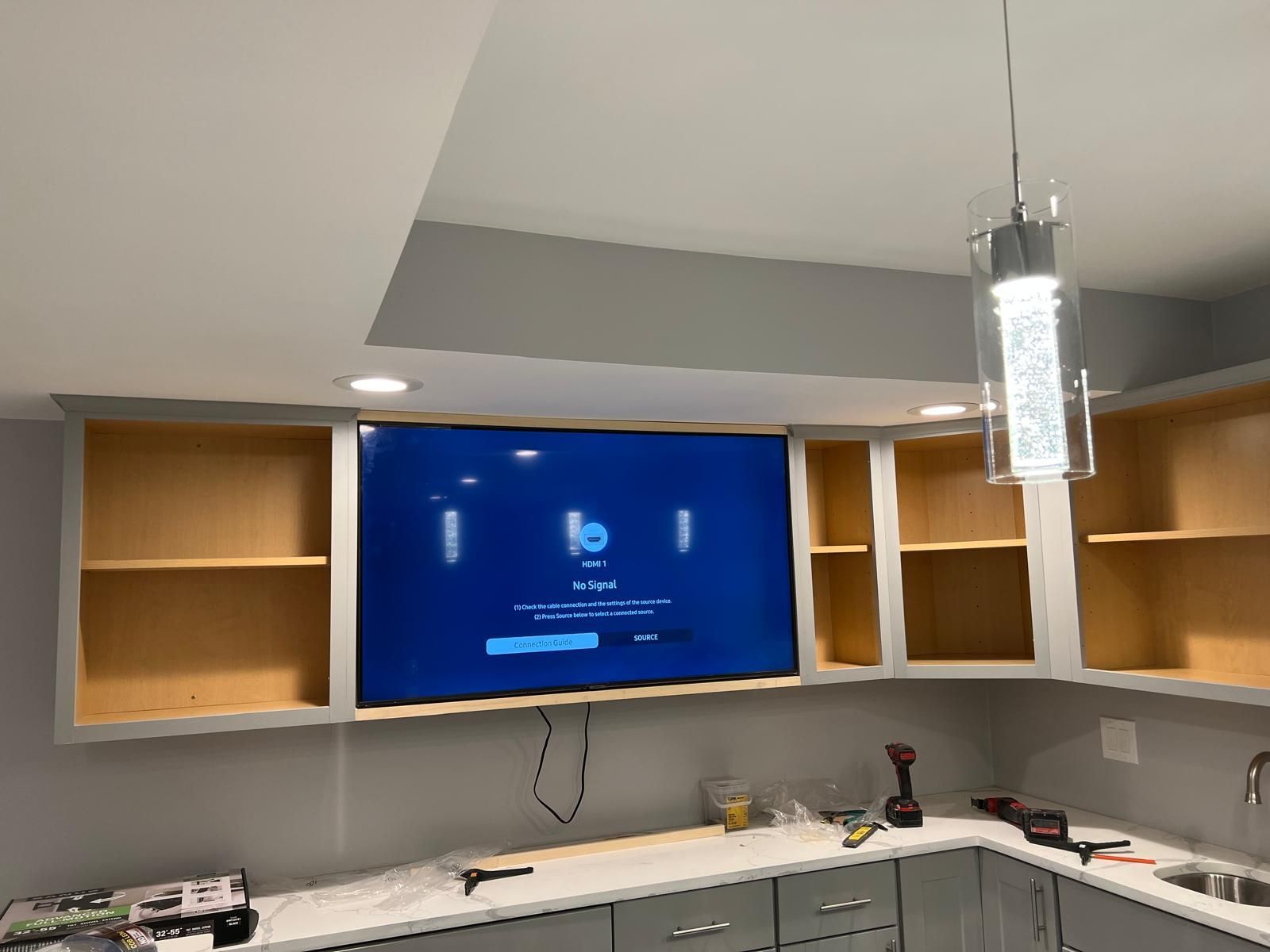 A kitchen with a flat screen tv hanging from the ceiling.