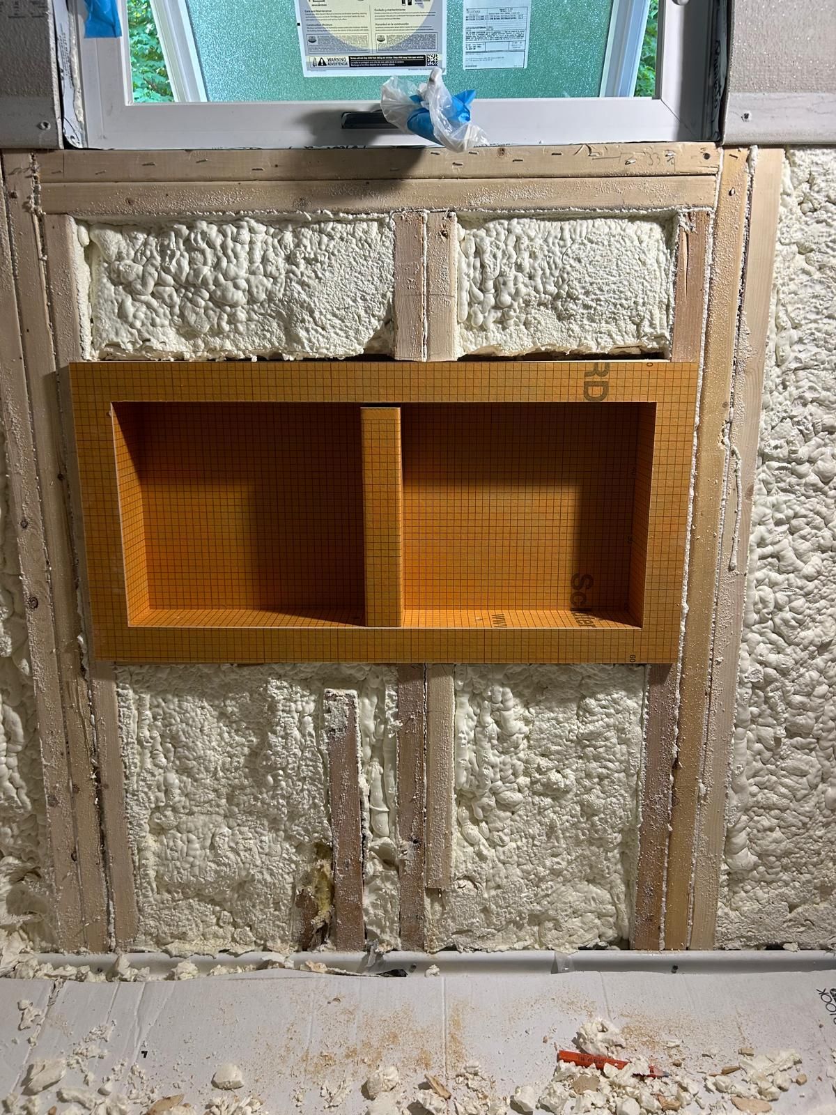 A wooden shelf is being built into a wall next to a window.
