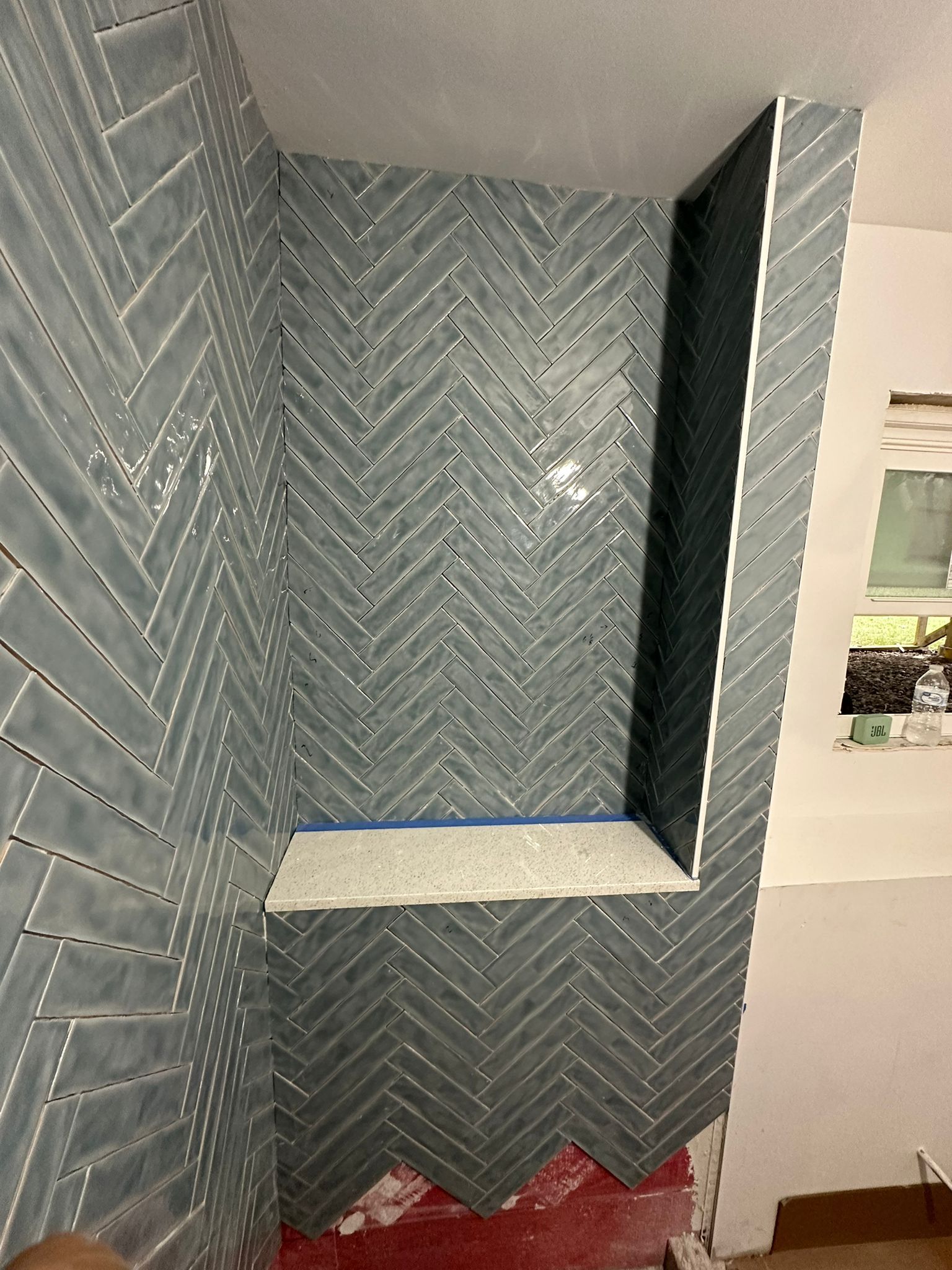 A bathroom with a herringbone tile wall and a shelf.