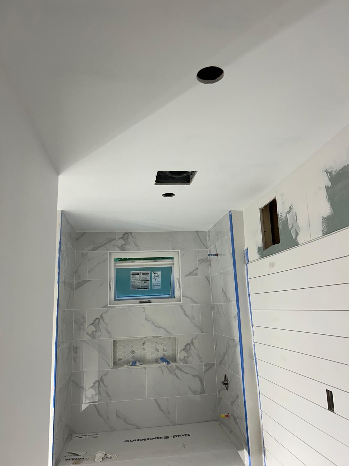 A bathroom under construction with white tiles and a window.