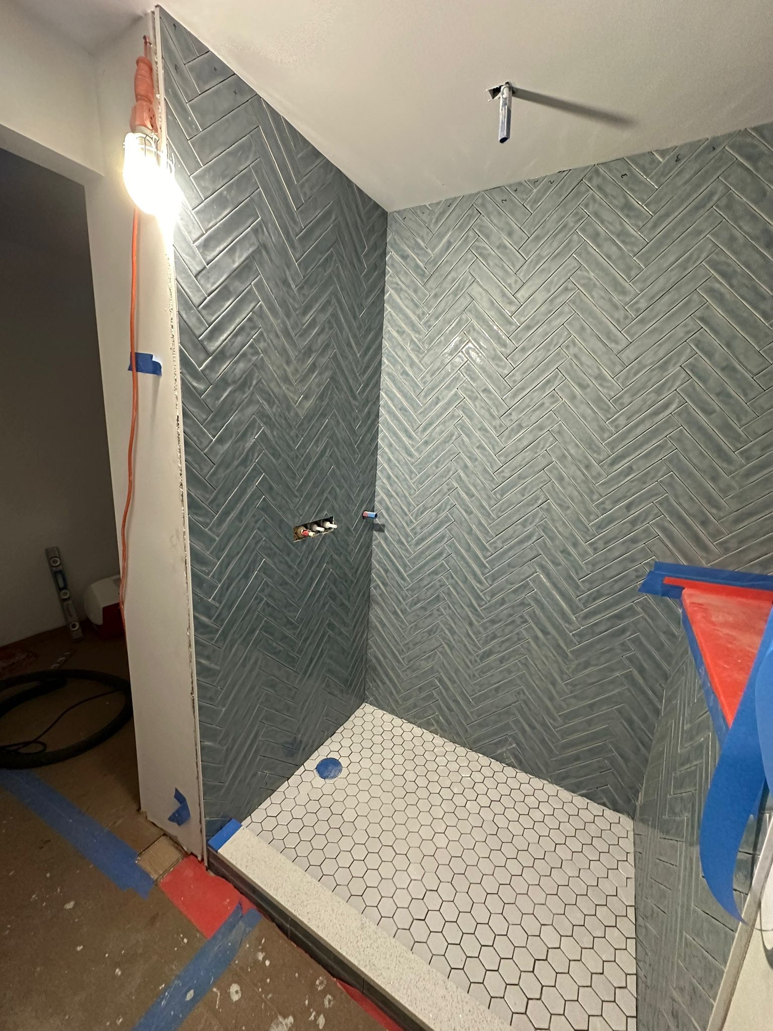 A bathroom with a walk in shower and a herringbone tile wall.