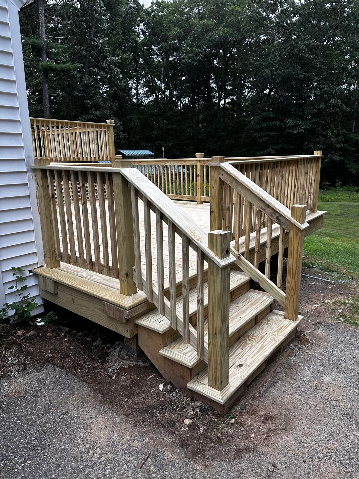 A wooden deck with stairs leading up to it is next to a white house.