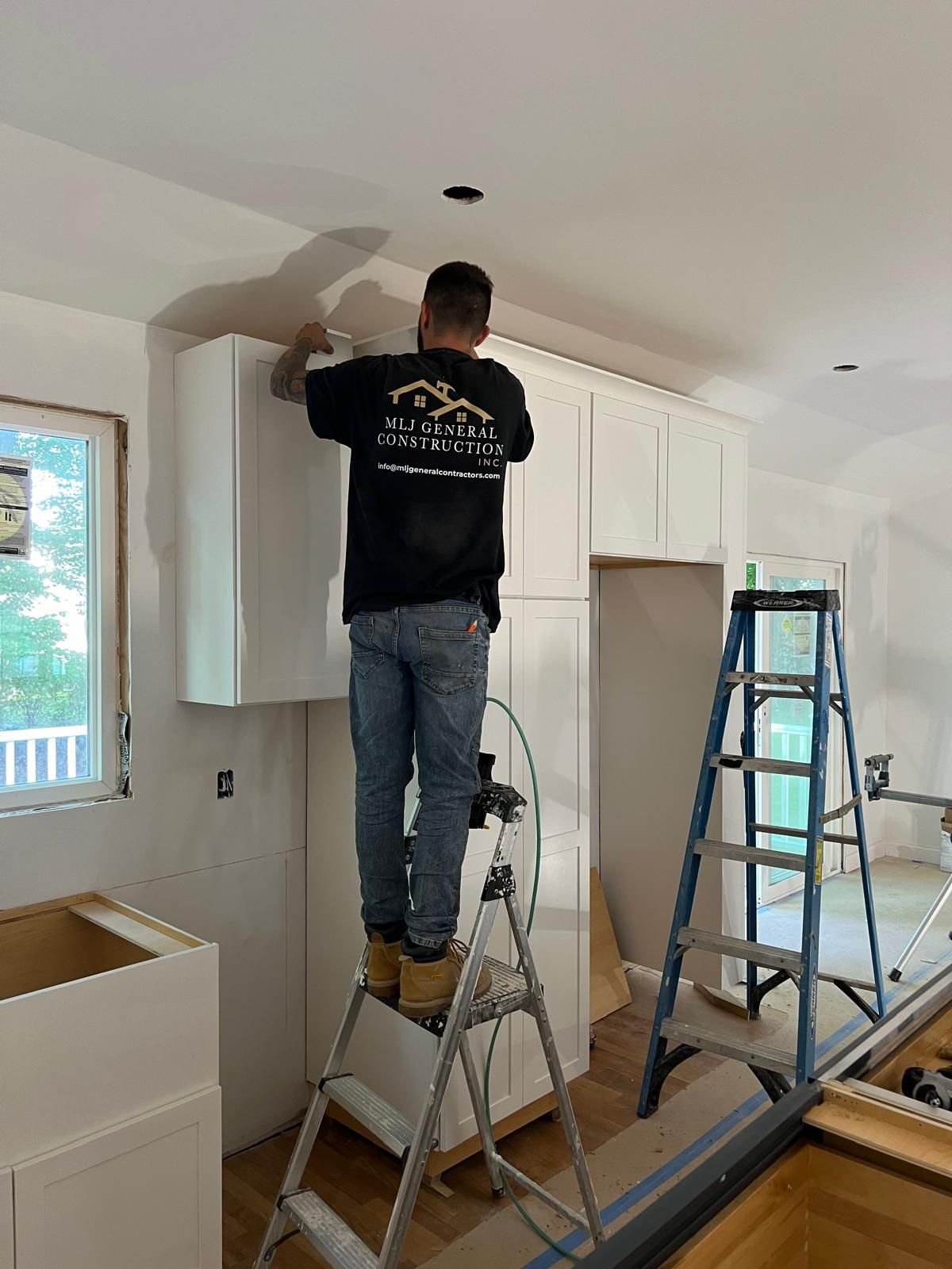 A man is standing on a ladder in a kitchen installing cabinets.