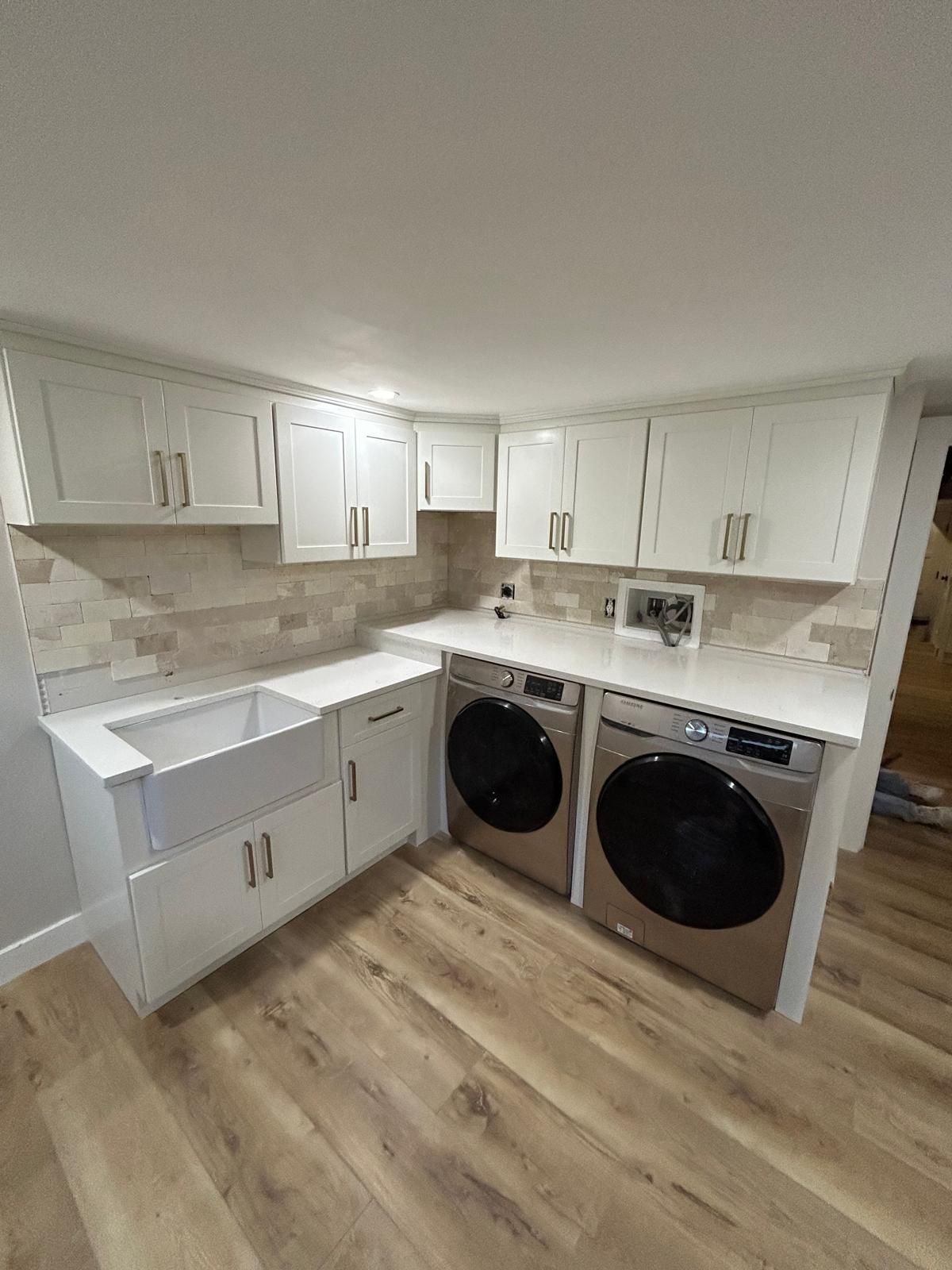 A laundry room with a sink , washer and dryer , and white cabinets.