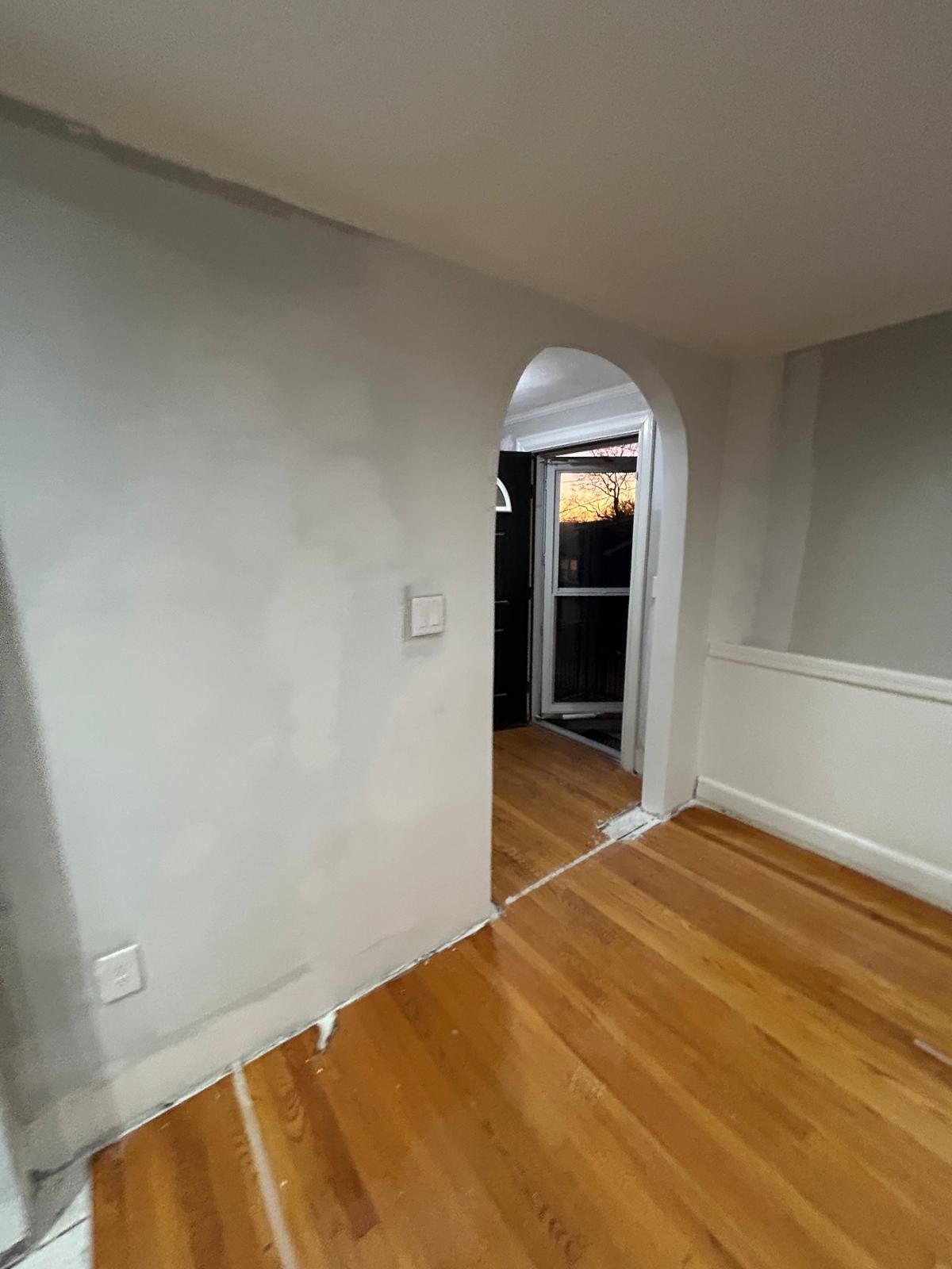 An empty room with hardwood floors and a white wall.