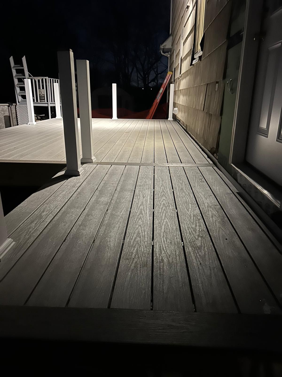 A wooden deck is lit up at night in front of a house.