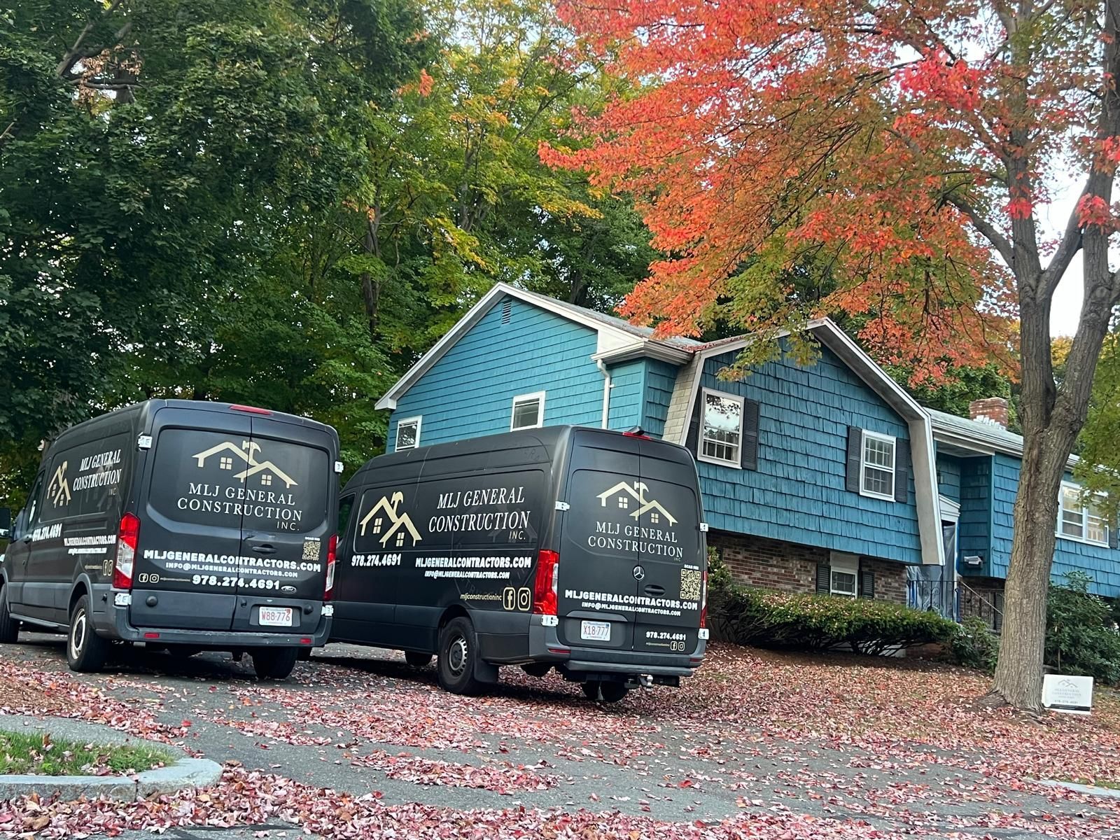 Two vans are parked in front of a blue house.