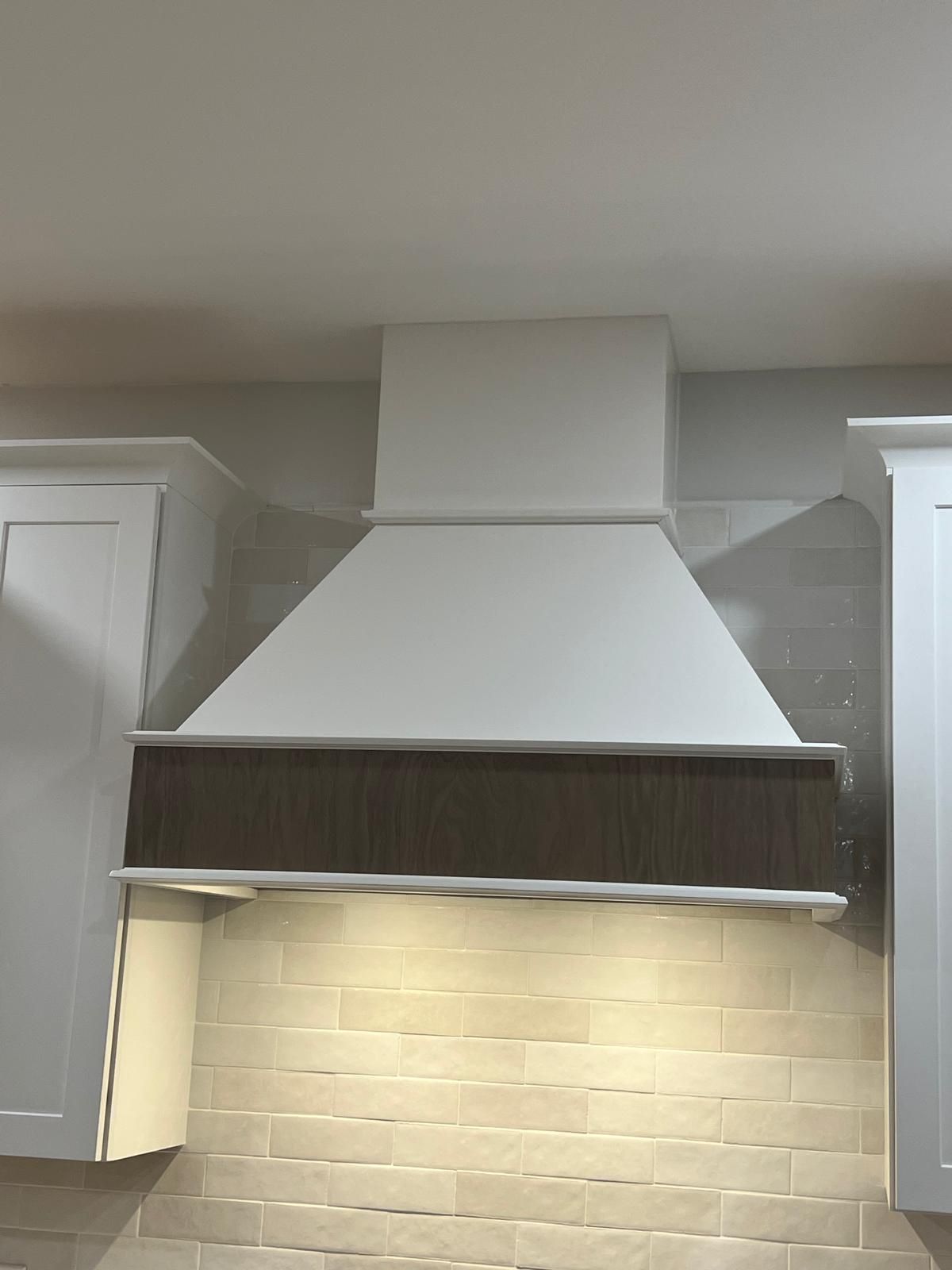 A kitchen with white cabinets and a white hood