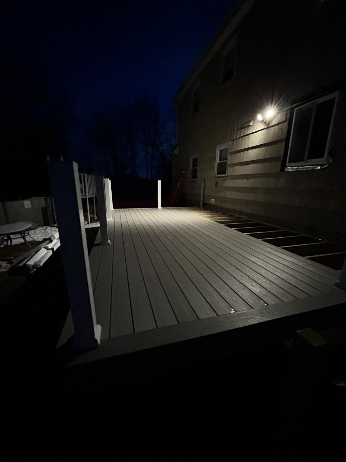 A wooden deck is lit up at night in front of a house.