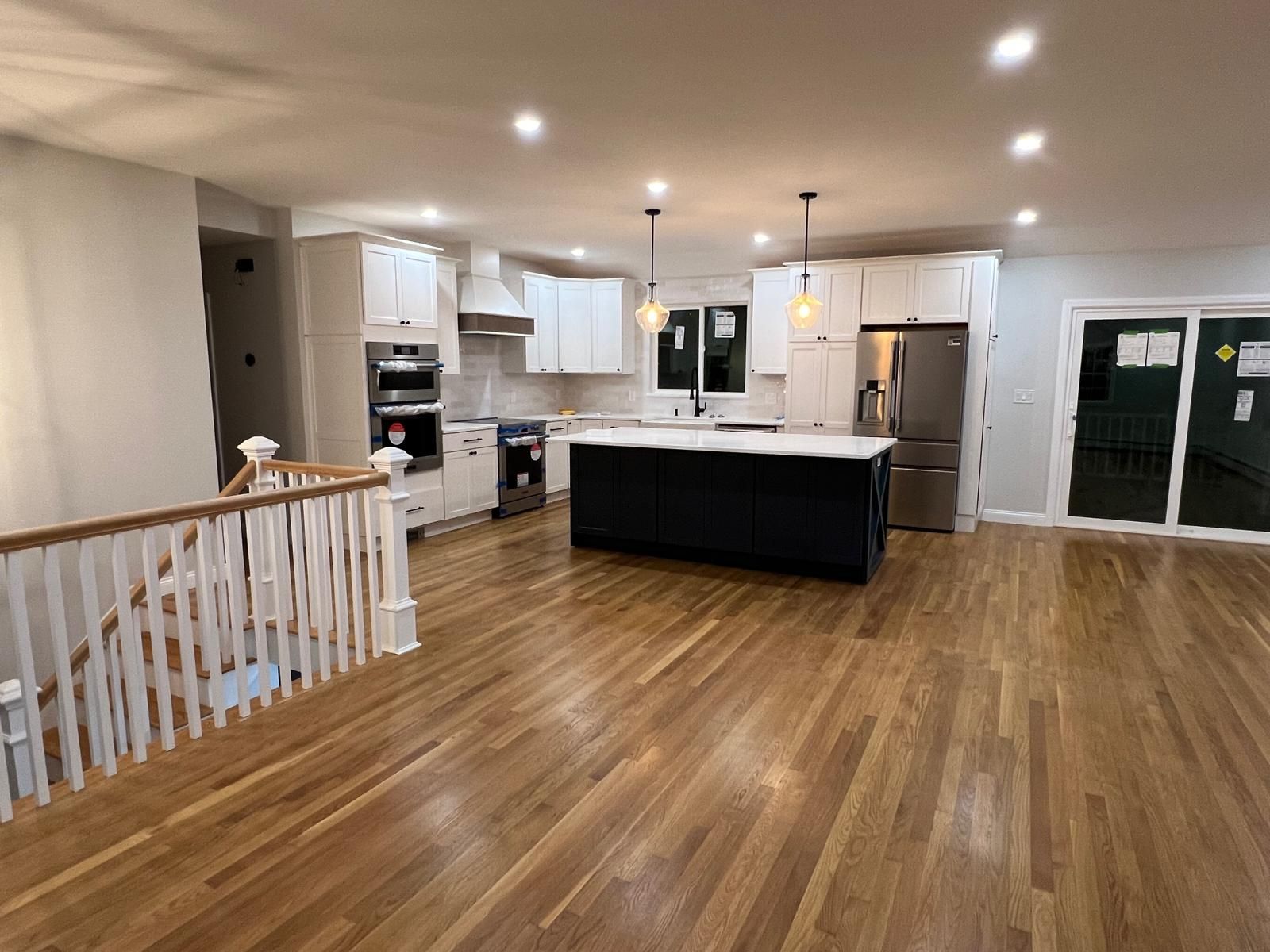 A kitchen with hardwood floors , white cabinets , stainless steel appliances and a large island.