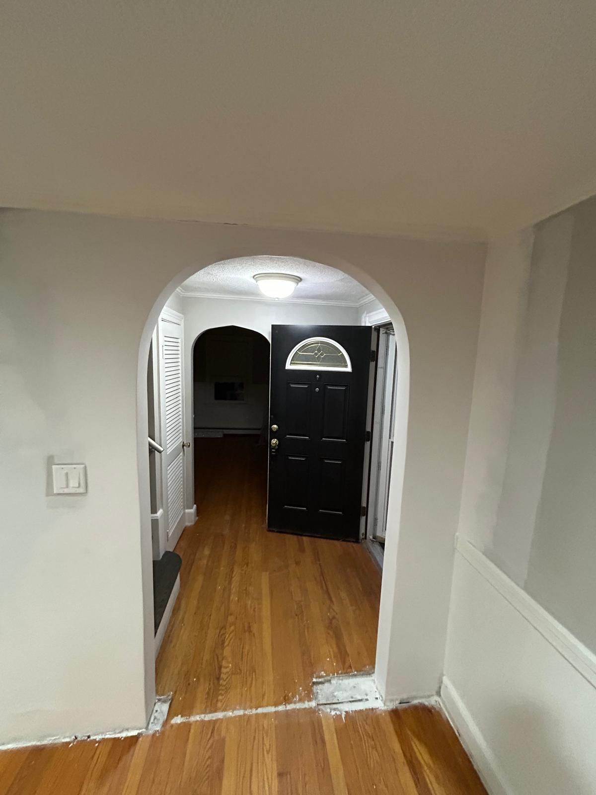 A hallway with a black door and wooden floors in a house.