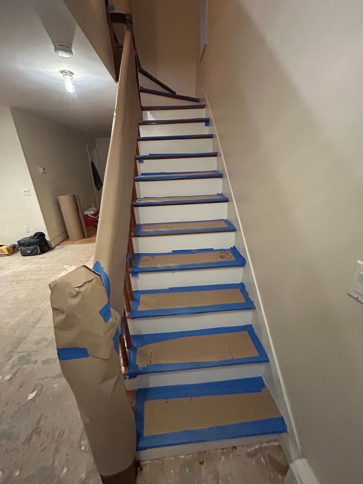 A staircase with blue tape on the steps is being painted.