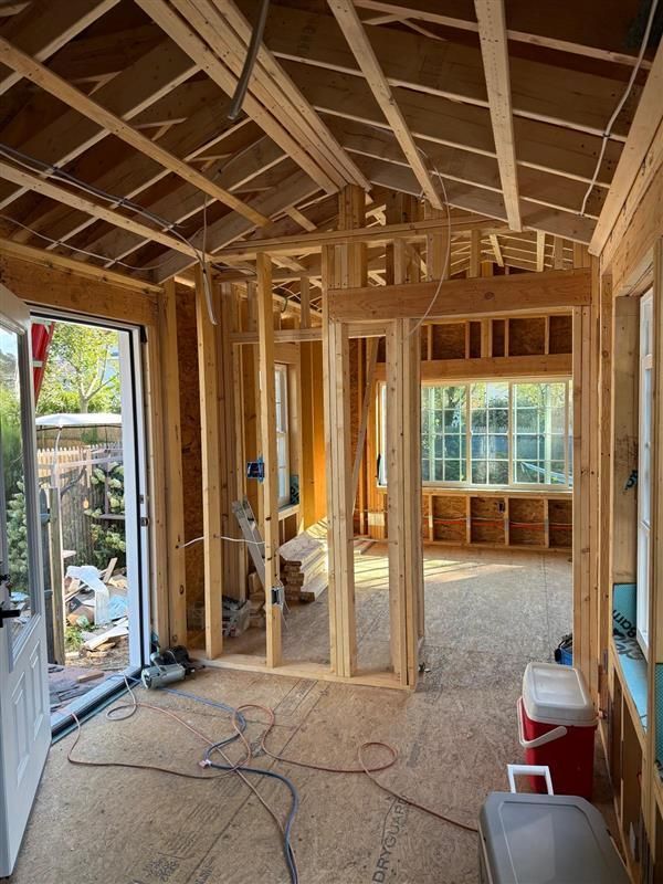 Interior view of a room under construction. Wood framing for walls and ceiling, with a door and windows visible.