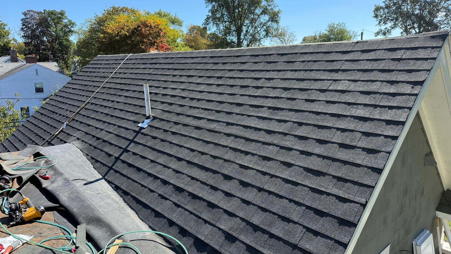 A dark shingle roof with a metal antenna, likely under construction with tools nearby.
