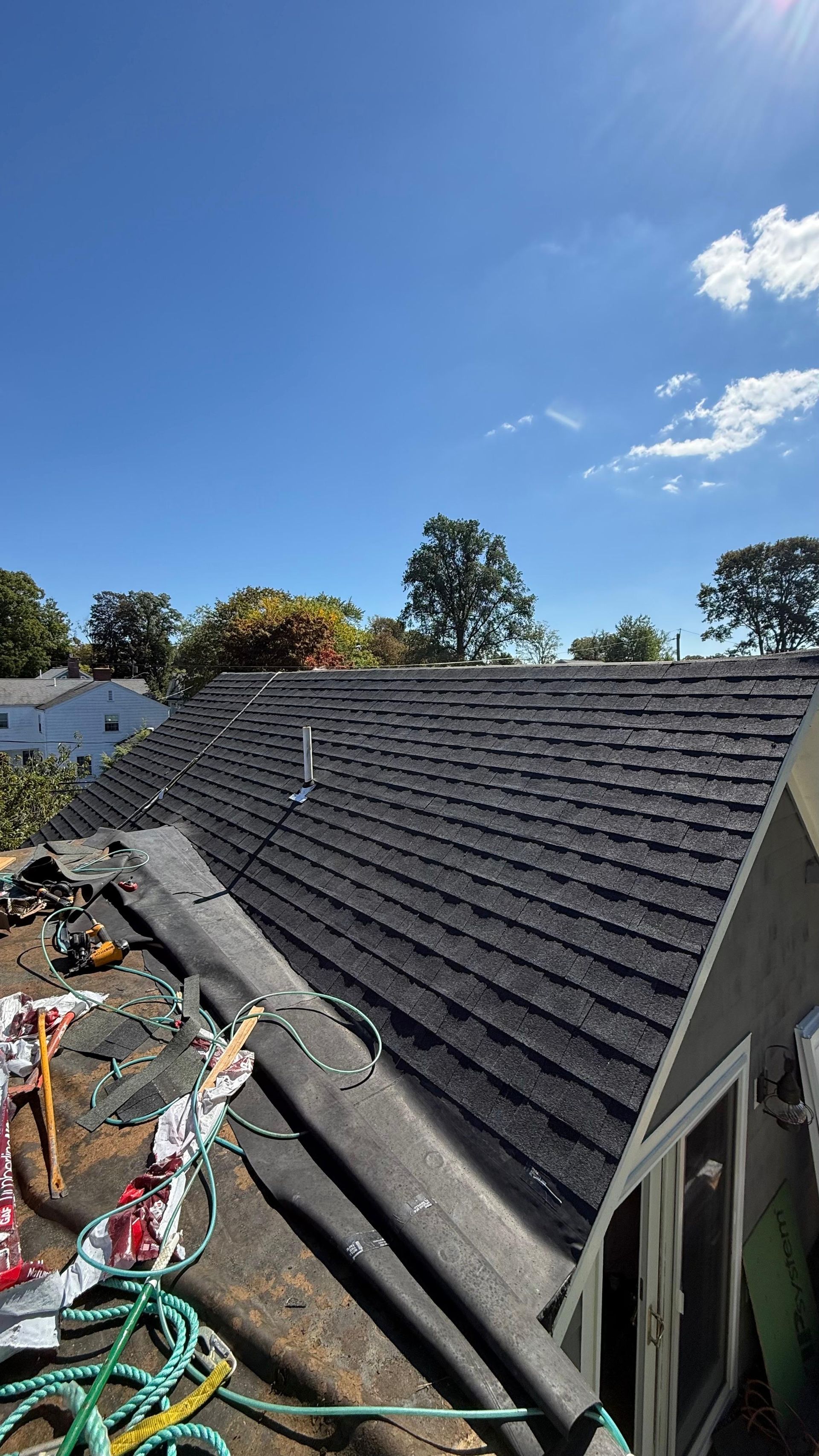Newly shingled dark roof with a partially torn up underlayer, under a bright blue sky.