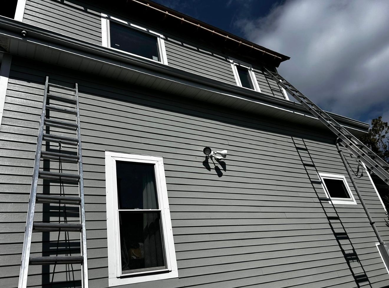 Gray house with ladders, cloudy sky. Security camera mounted on the side.
