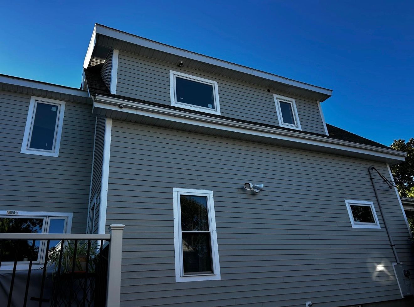 Side view of a two-story house with gray siding, white trim, and windows, against a blue sky.