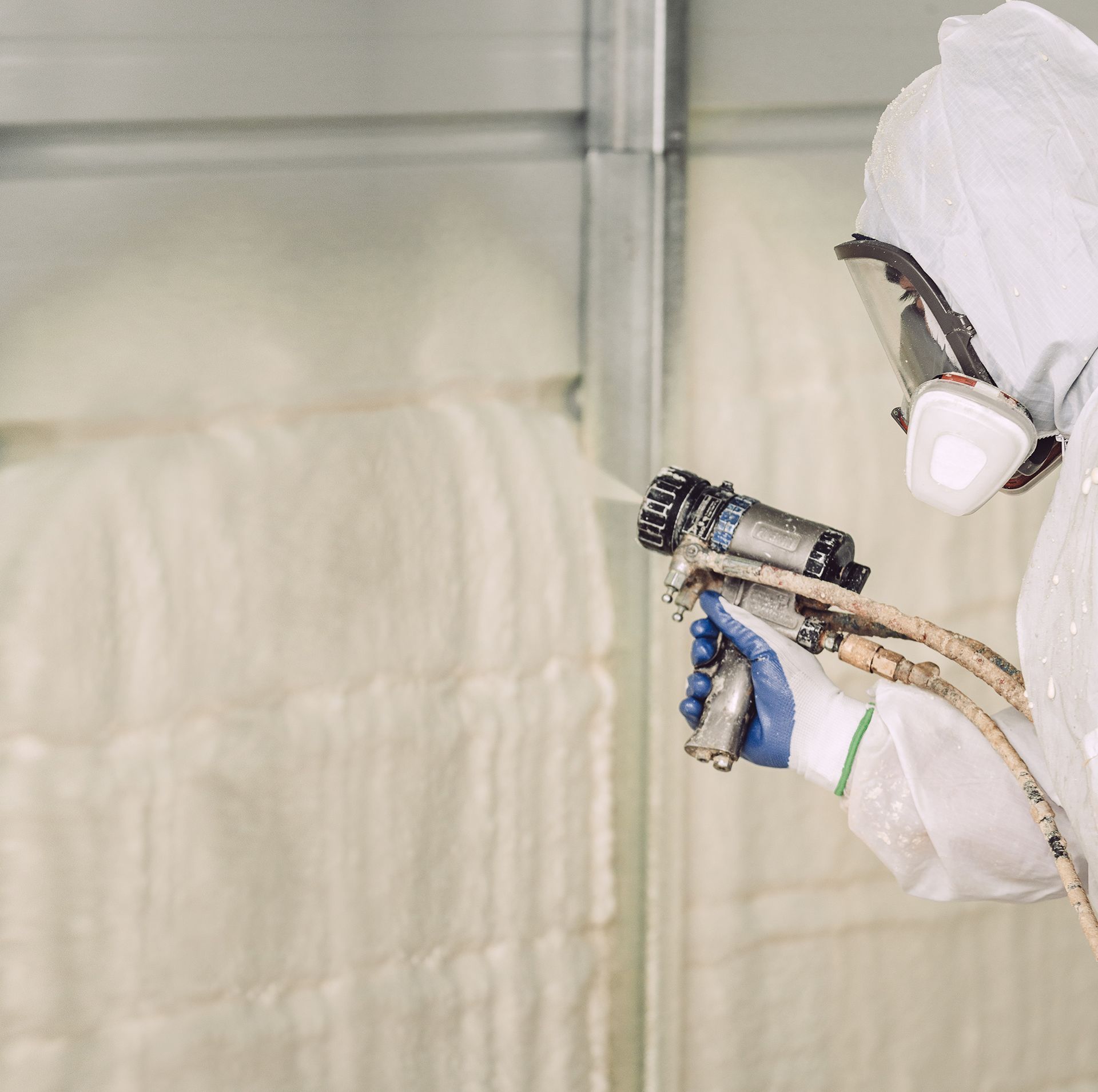 Person in protective suit spraying insulation on a wall.