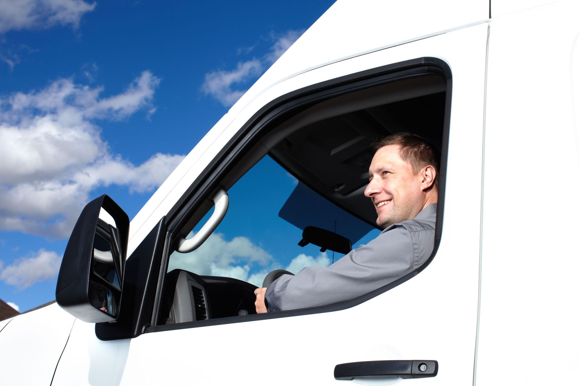Smiling person driving a white truck on a sunny day.