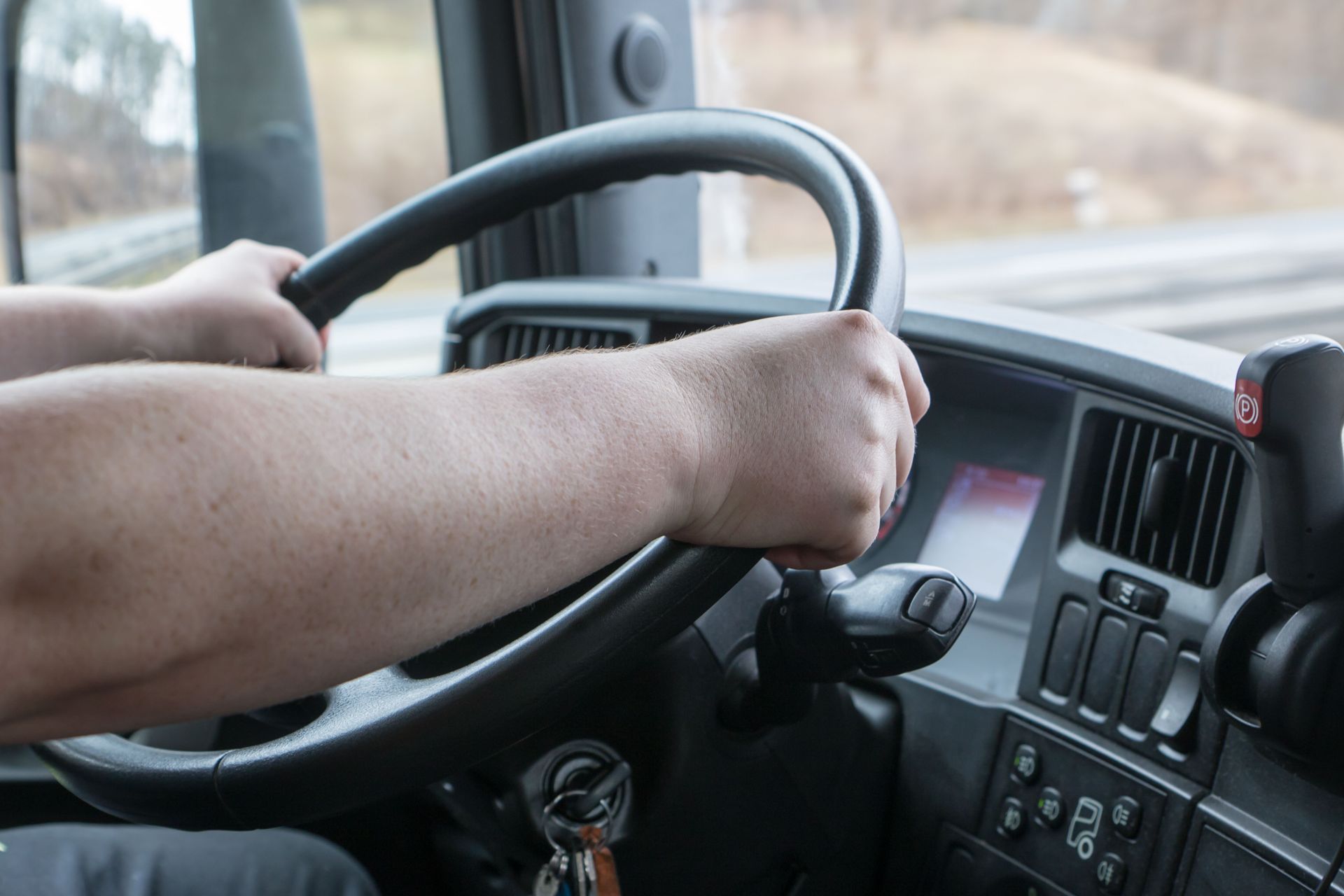 Hands gripping steering wheel inside a truck cab, driving on a road.