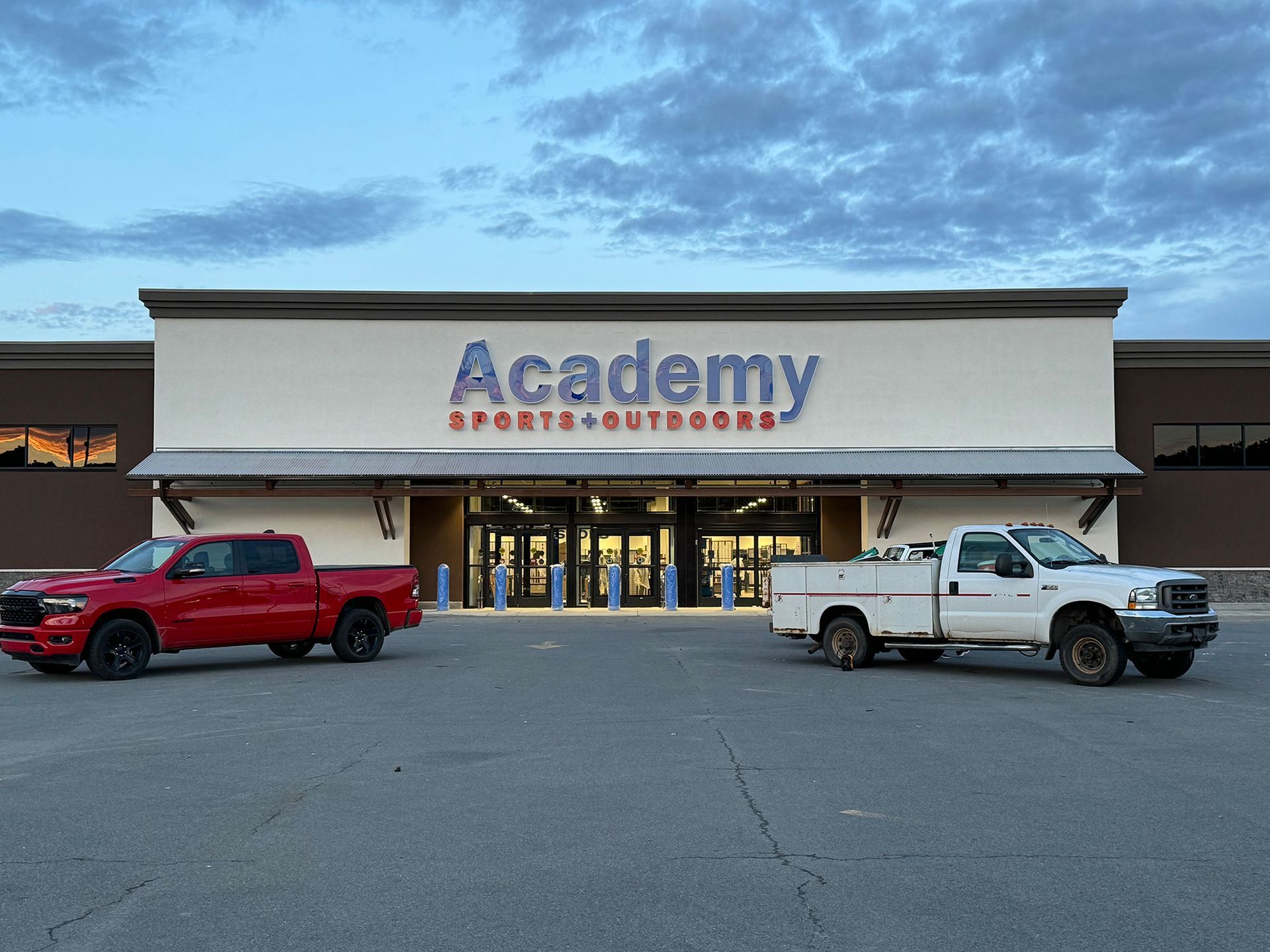 Two trucks are parked in front of an Academy store.