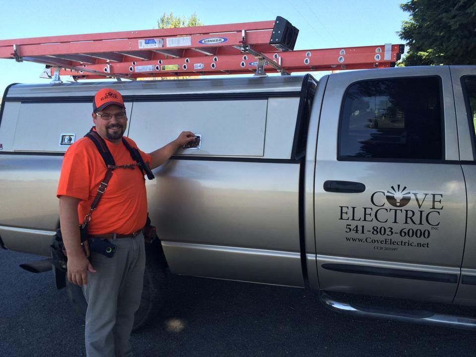 A man standing next to a silver truck that says cove electric