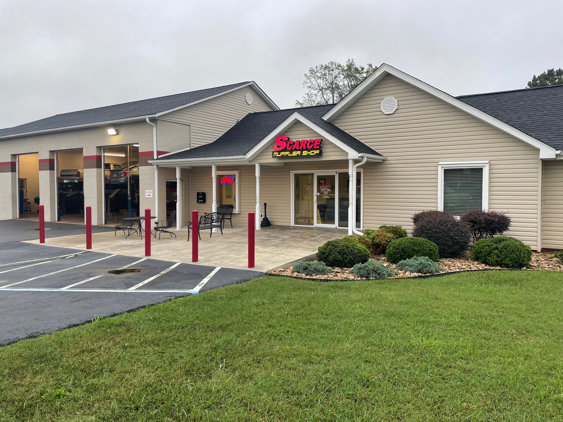 Exterior view of a car repair shop. Beige building with red trim, grass, and a paved parking lot. 
