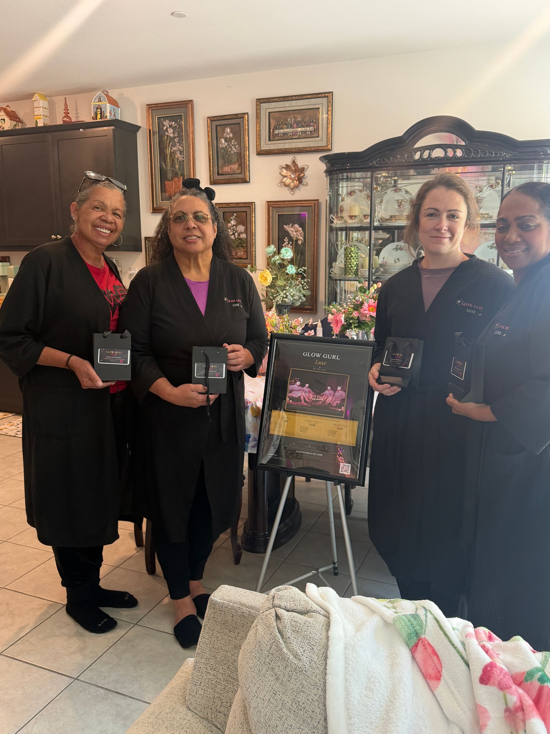 Four people in black attire hold plaques in a decorated room with framed art and flowers.