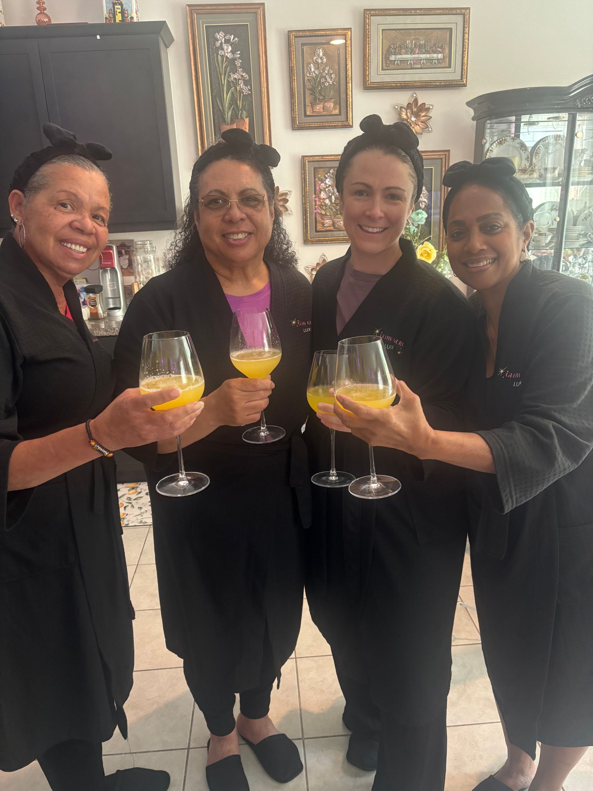 Four people in black outfits smiling and holding drinks indoors at a gathering