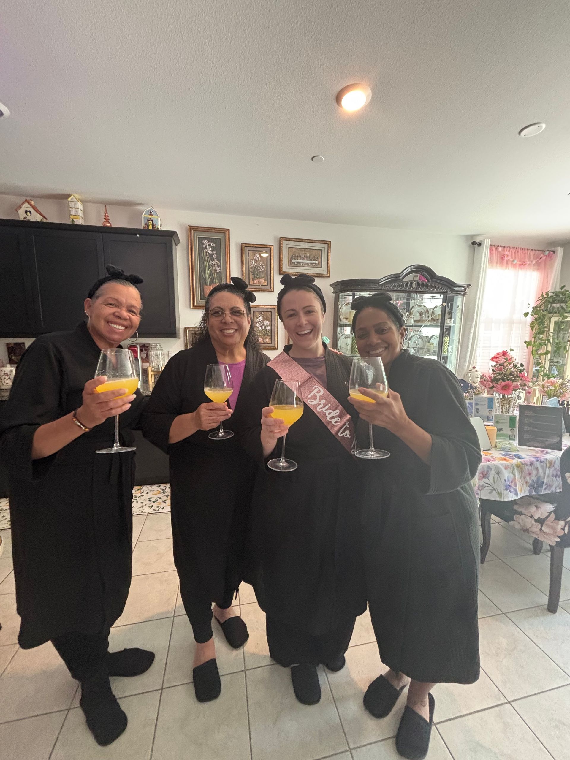Four people in black outfits smiling and holding colorful drinks at an indoor gathering