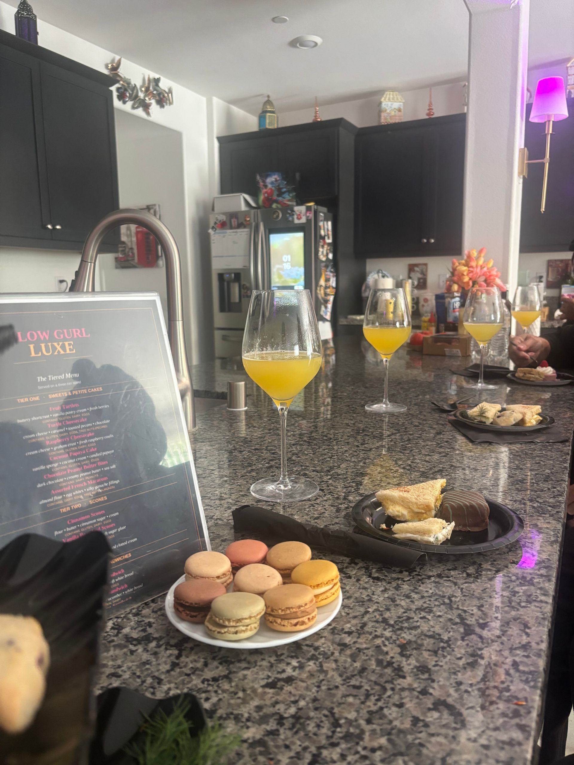 Kitchen counter with colorful macarons, pastries, and orange drinks on a granite island.