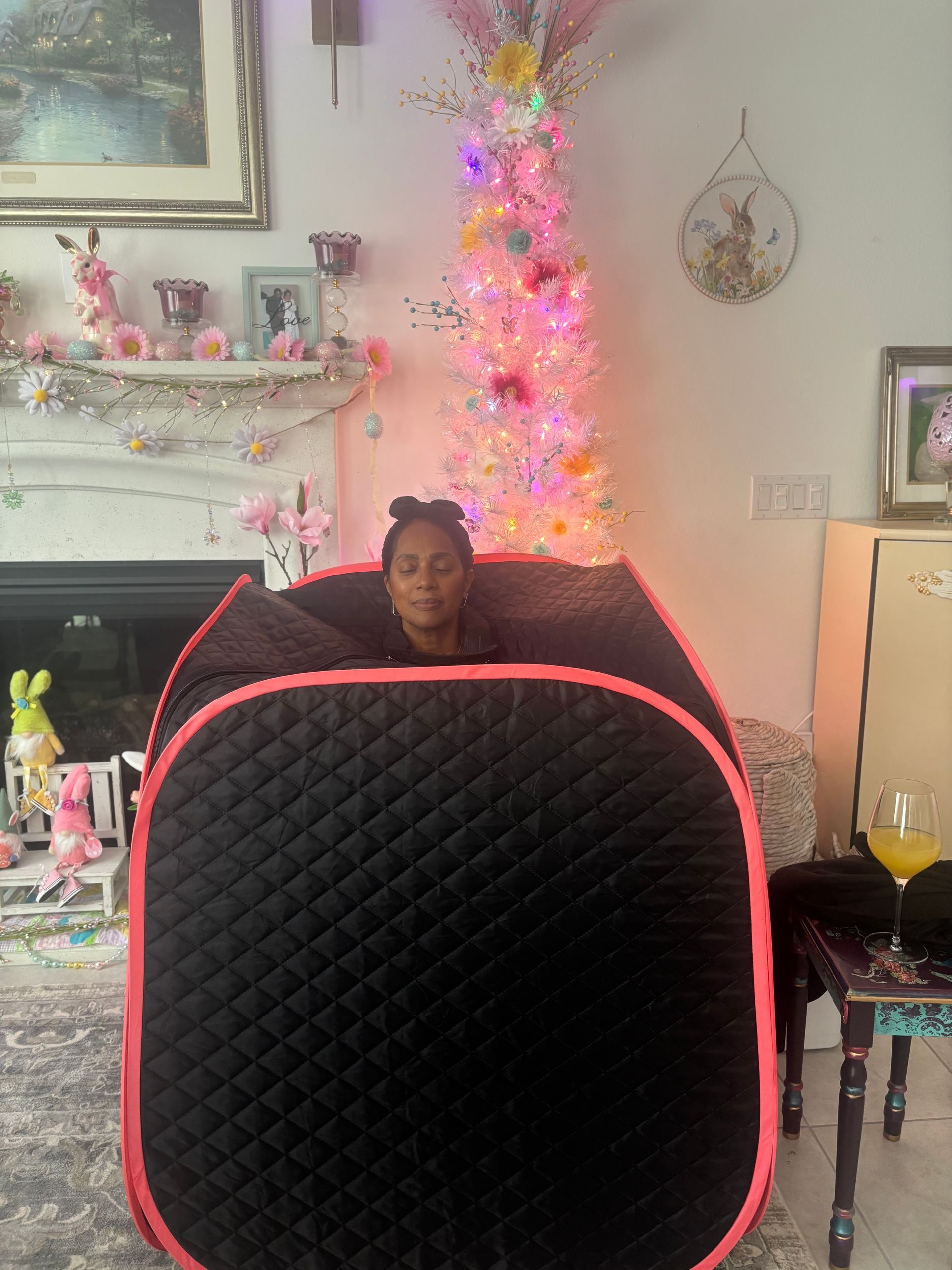 Person seated behind a large black-and-pink cushion in a decorated living room with a lit pink Christmas tree