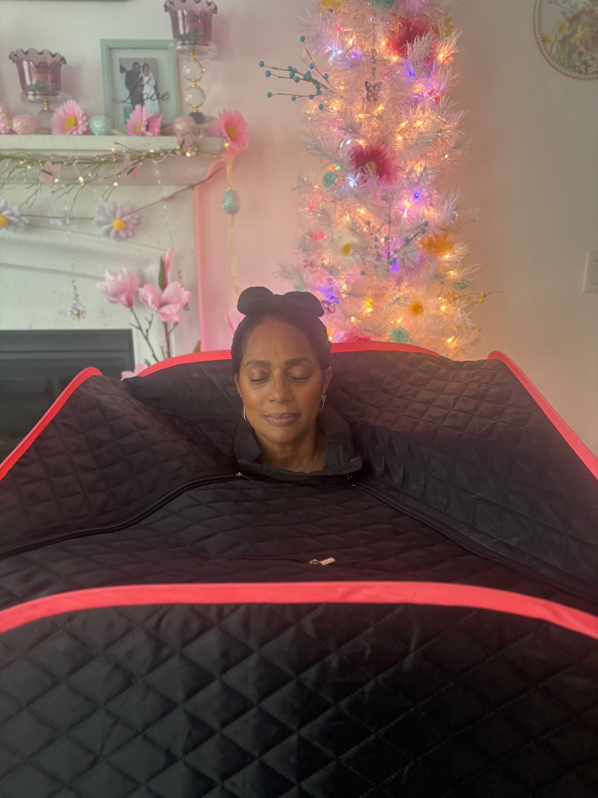 Person resting under a black quilted blanket with red trim in a cozy room lit by colorful lights.