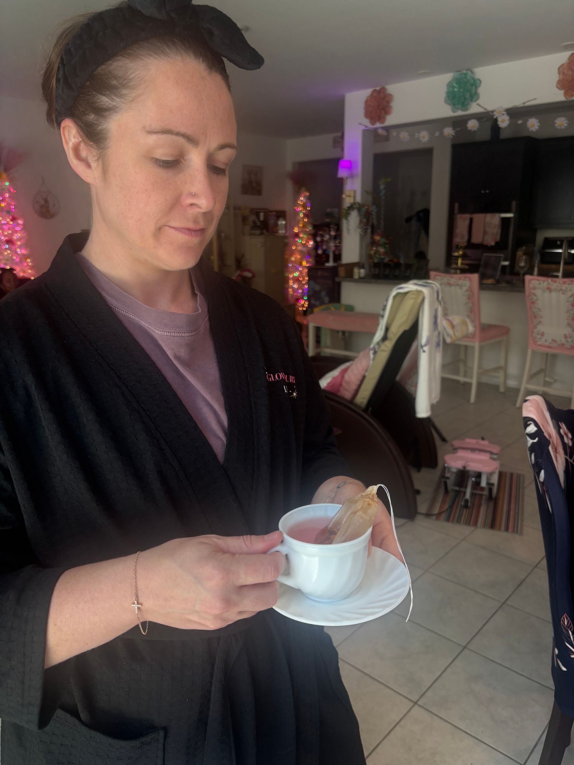 Woman holding a cup and saucer in a cozy kitchen with holiday lights in the background