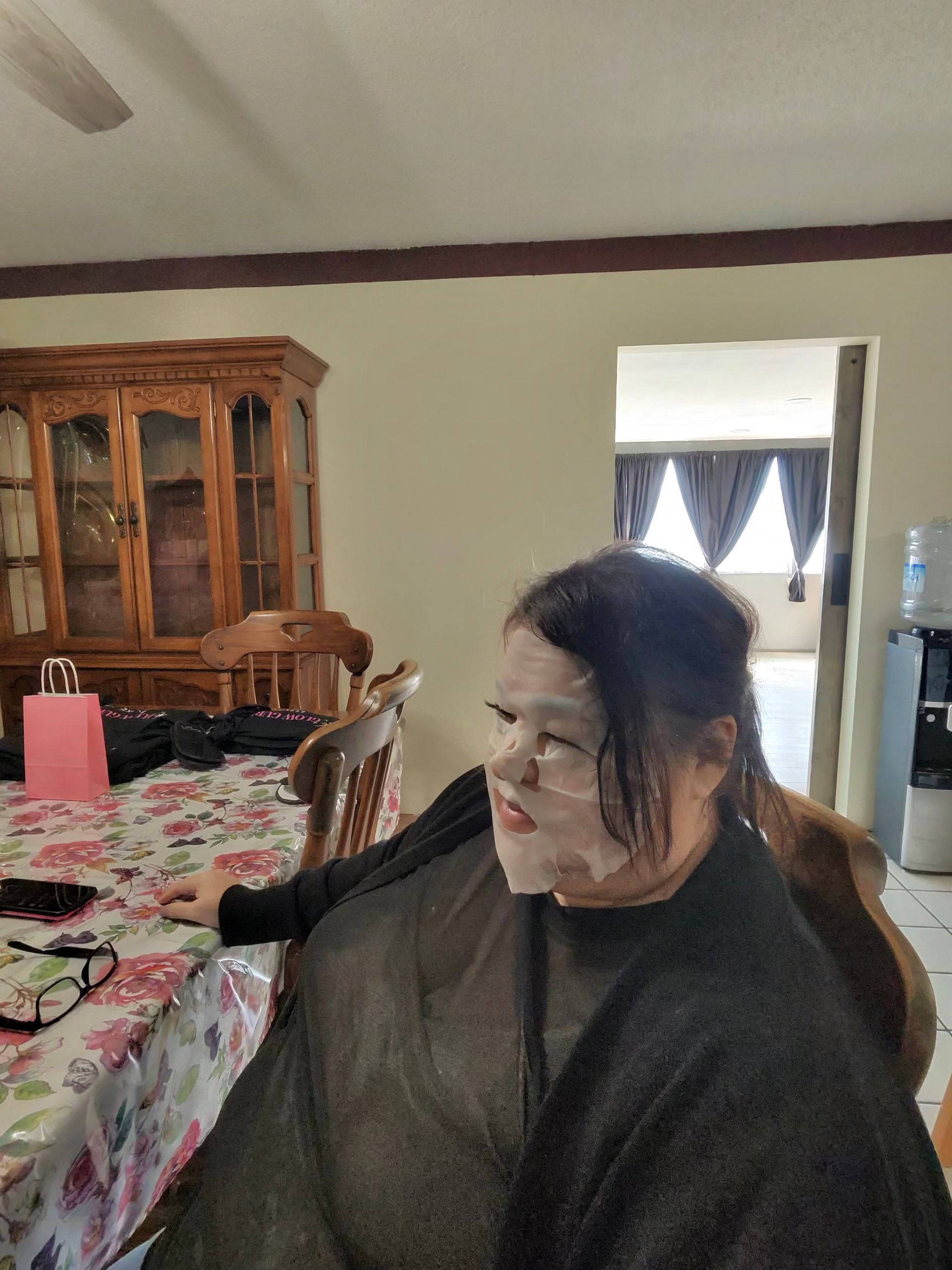 Person seated at a dining table in a home, wearing a dark sweater and looking to the side.