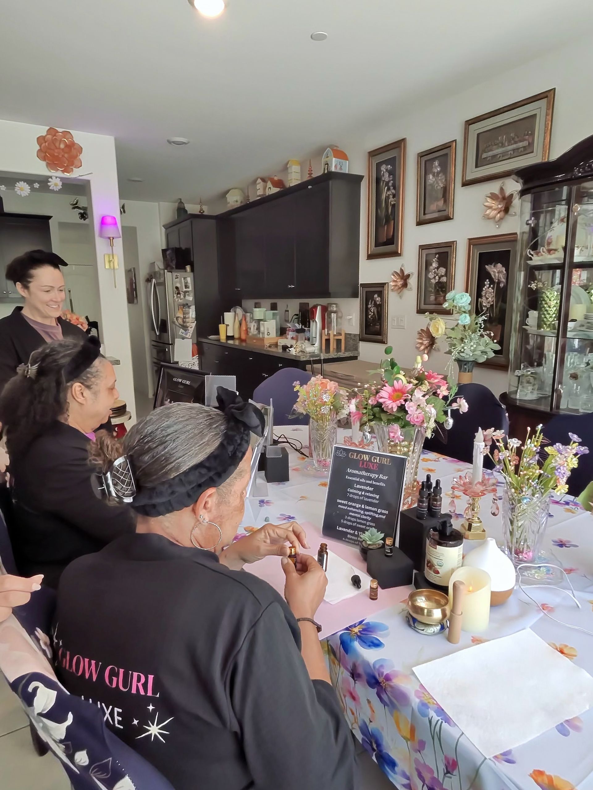People seated at a decorated table in a home, facing a wall of framed photos and art.
