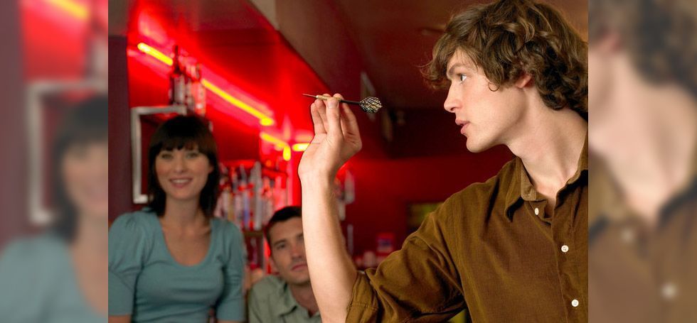 A man is holding a dart in his hand in a bar.